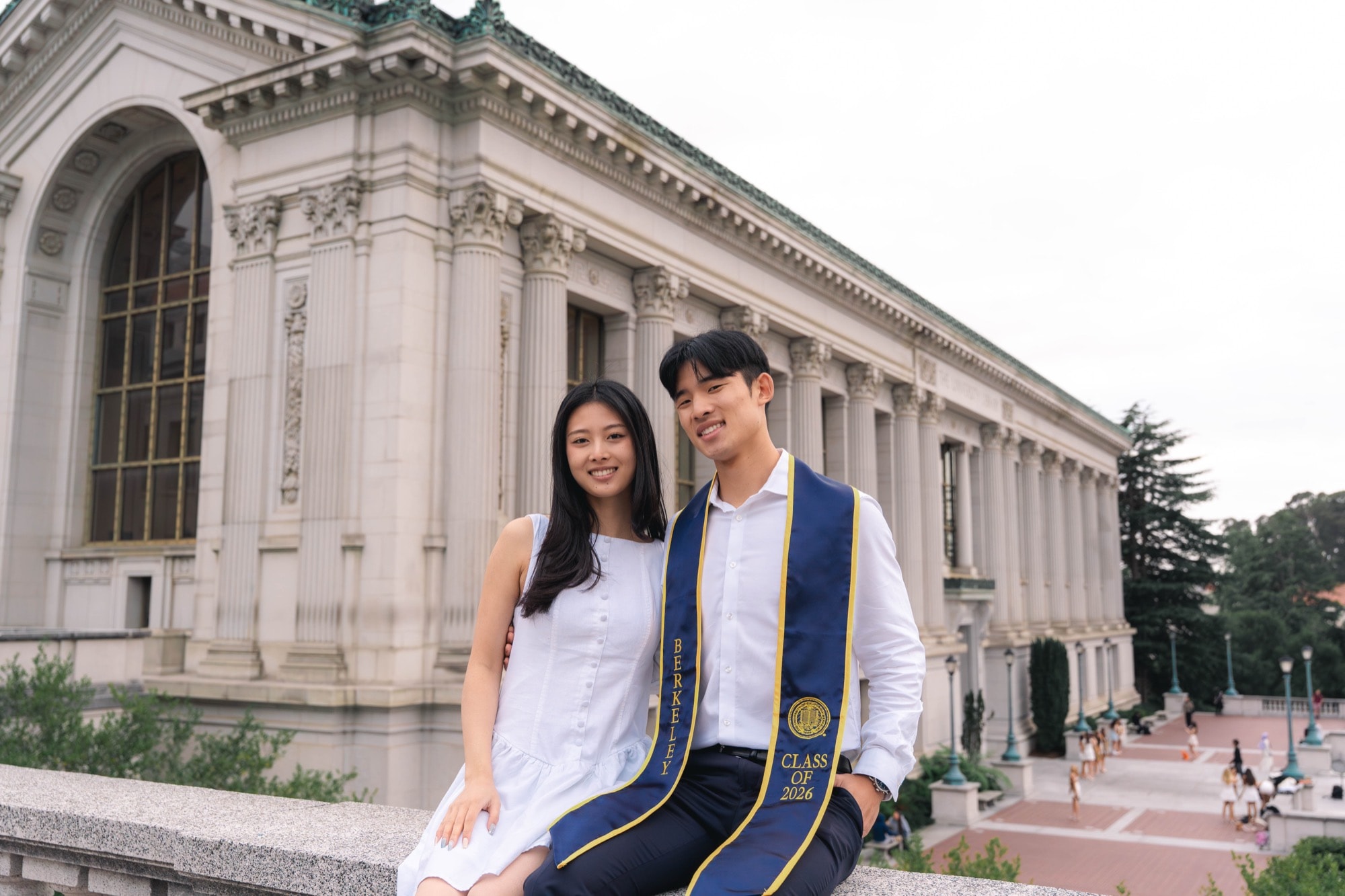 Two graduates seated together before Doe Library