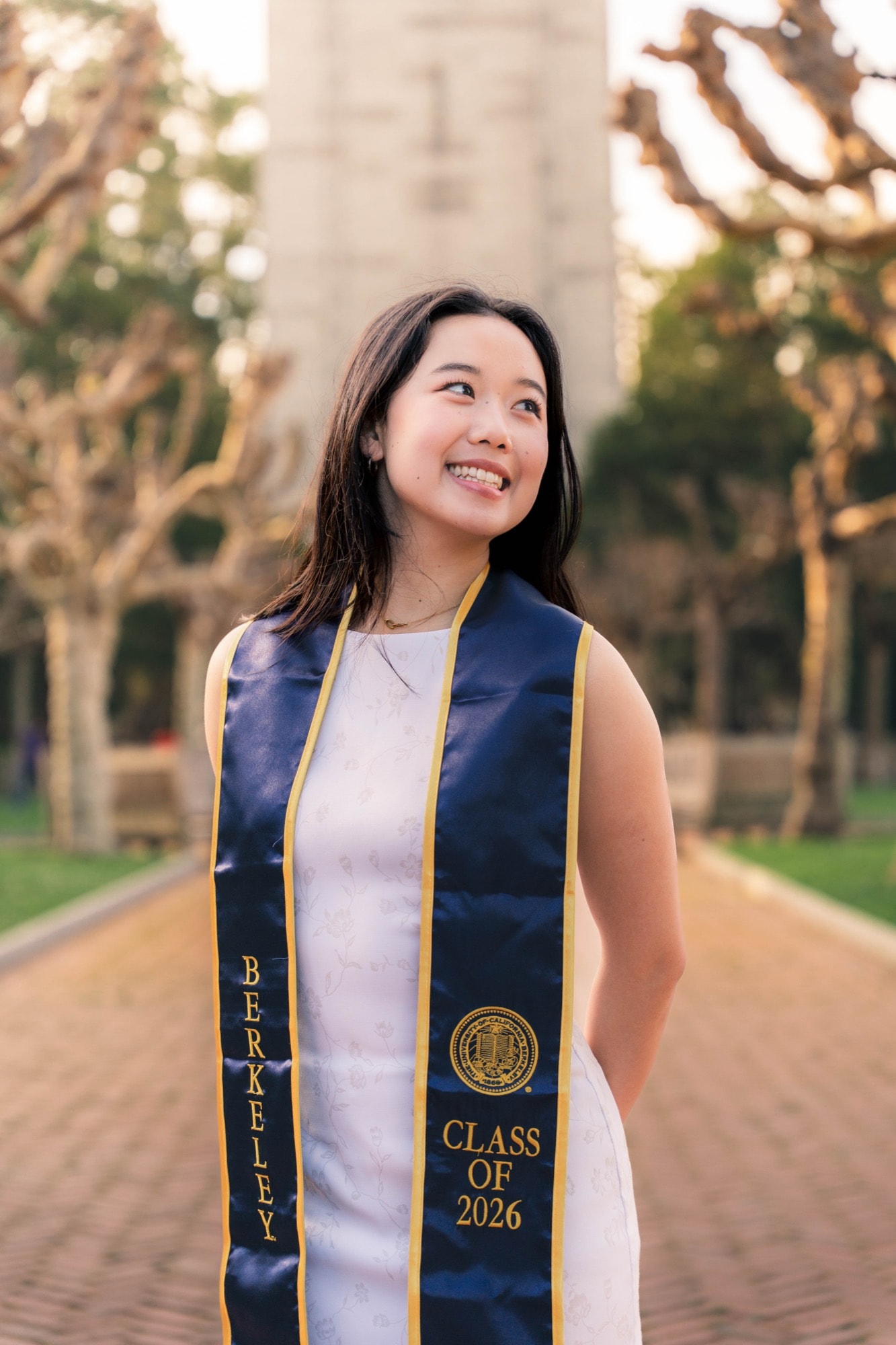 Graduate looking up and smiling, the Campanile glowing at sunset