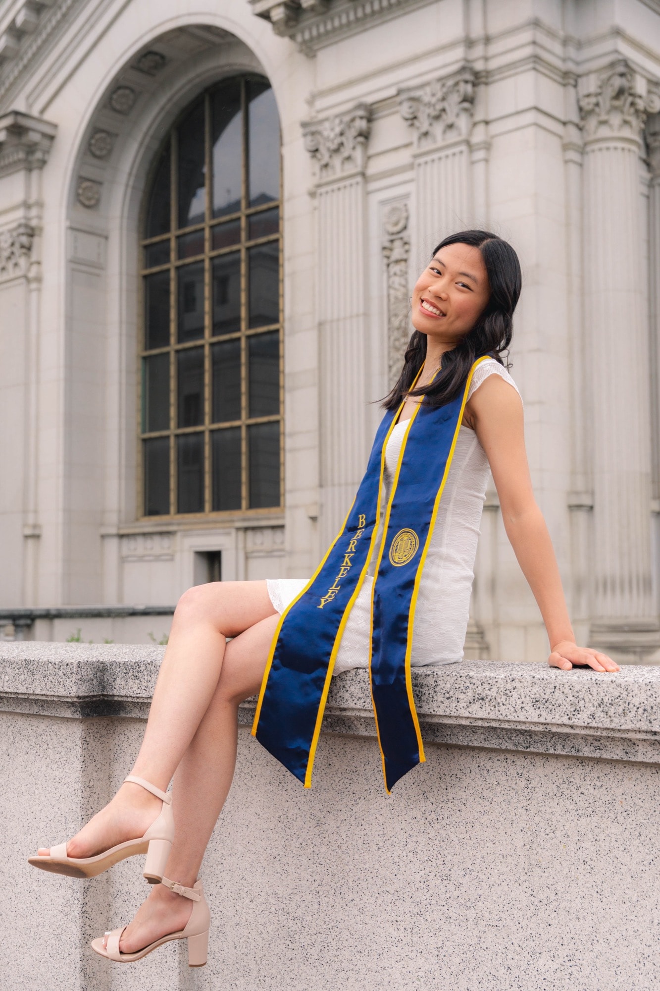 Graduate laughing on a stone railing, ornate facade behind