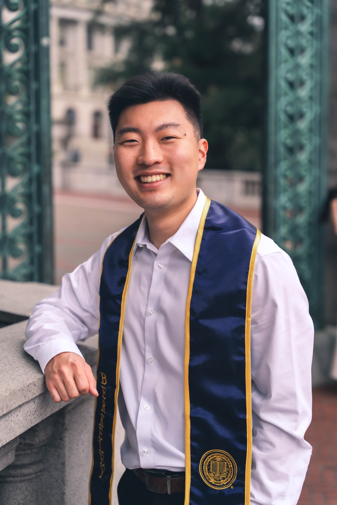 Graduate leaning on a railing near Sather Gate, smiling